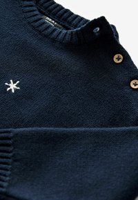 Tamsiai mėlynas megztinis su gipiūro apykakle ir rankogaliais, su mažąja balta išsiuvinėta žvaigžde ir dviem mediniais mygtukais ant peties.