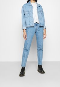 Hellblaues Denim-Jackett mit Kragen, zwei Brusttaschen und Knopfverschluss. Kombiniert mit hellblauen Jeans und schwarzen Schnürboots.