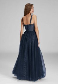 Robe de soirée bleu marine avec un corsage ajusté, des fines bretelles et une jupe fluide en tulle ornée d'accents scintillants, mettant en valeur un dos ouvert.