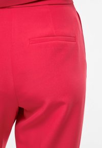 Gros plan sur un pantalon rouge vif sur mesure montrant une poche passepoilée à l'arrière du côté droit.