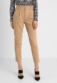 Beige højtaljede tapered bukser med frontfolder, båret med sorte spidse hæle og en langærmet top med sort-hvide mønstre.