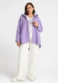 Giacca a zip viola con cappuccio e cordini, in un fit rilassato, abbinata a una t-shirt viola chiaro e pantaloni bianchi a zampa.