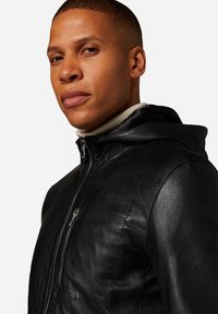 Schwarze Lederjacke mit Kapuze, ausgestattet mit einem Reißverschluss und einer strukturierten Oberfläche. Die Jacke hat eine glatte Oberfläche und dezente Nähte.