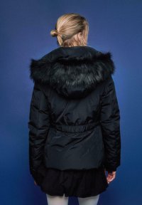 Črna puhasta jakna s kapuco iz umetnega krzna, z zategnjenim pasom in dolgimi rokavi. Gladek tekstura z bleščečim zaključkom na modrem ozadju.