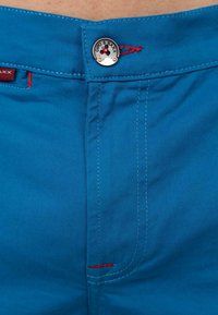 Blauwe katoenen shorts met rode stikaccenten en een metalen knop met een logo. Gladde textuur, gestructureerd ontwerp, medium hoogte pasvorm.
