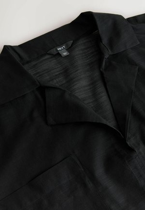 Crna košulja s ovratnikom, prsni džep i etiketa marke "NEXT" zašivena na unutarnjoj strani ovratnika.