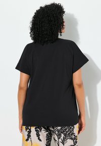 Musta lyhythihainen t-paita rentoa istuvuutta, valmistettu pehmeästä kankaasta; selässä on yksinkertainen muotoilu ilman koristeita tai kuvioita.