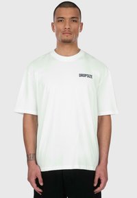 Weißes Baumwoll-T-Shirt mit kurzen Ärmeln, Rundhals und einem kleinen schwarzen "DROPSIZE"-Logo auf der linken Brustseite. Normale Passform.