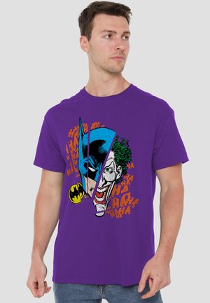 Man wearing purple T-shirt featuring split face graphic of Batman and Joker with orange "HA HA" text background.