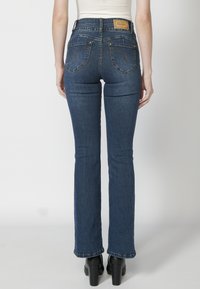 Dark blue flared jeans with a high waist, visible stitching, and two back pockets. Features a leather logo patch on the waistband.