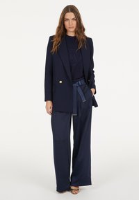 Navy blazer with gold buttons, paired with a navy sweater featuring a logo, and wide-leg satin pants with a tied waistband.