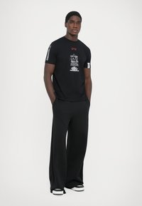 Black short-sleeve t-shirt with graphic print and white accents, paired with wide-leg black pants and black footwear with white soles.