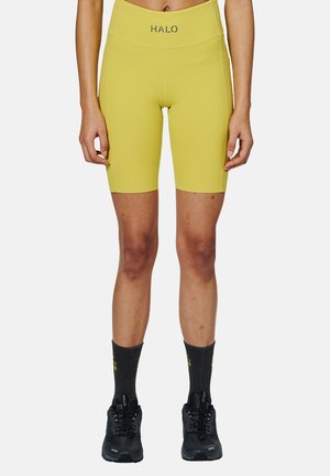 Gule cykelshorts med høj talje og "HALO" logo. Båret med sorte træningssko og mørke sokker med gult tekst.