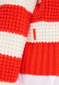 Gestreifter Pullover in Rot und Weiß. Dickes, strukturiertes Material mit einem gerippten unteren Saum. Verfügt über ein kleines Etikett mit der Aufschrift "MARCEIN SPORTS".