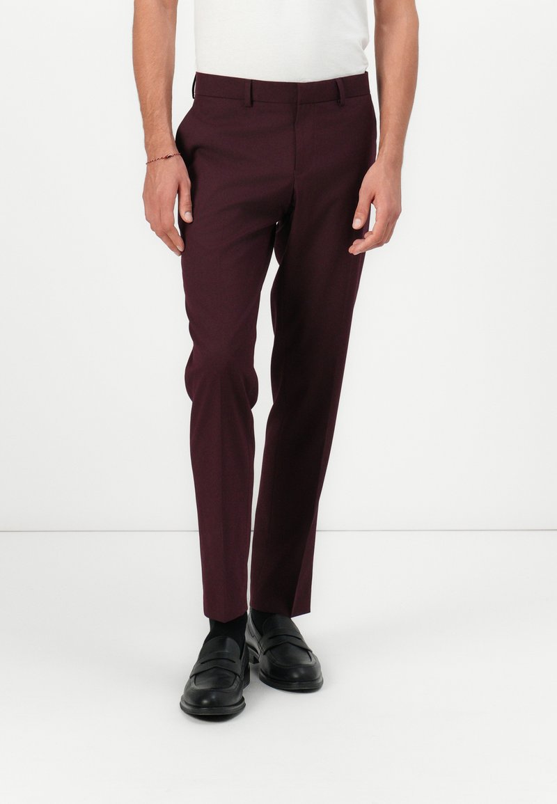 Burgundifarbenes, maßgeschneidertes Hosenpaar mit glatter Textur, slim fit und Gürtelschlaufen, kombiniert mit schwarzen Loafers und einem weißen Hemd.