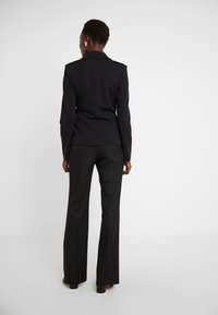 Svart skräddarsydd kavaj med axelaccenter och matchande utsvängda byxor. Slät tyg med en elegant design, sedd bakifrån.