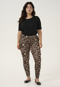 Haut noir à manches courtes associé à des leggings imprimés léopard aux teintes de marron et de crème. Accessoirisé avec des ballerines noires simples.