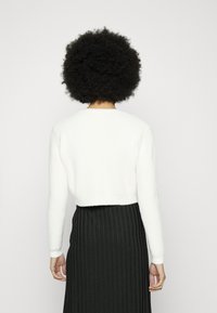 Weißer, kurz geschnittener Pullover mit strukturiertem Finish, Rundhalsausschnitt und langen Ärmeln, kombiniert mit einem schwarzen, senkrecht gerippten Rock.