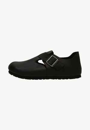 Black, molded clogs with a rounded toe, side cutout, strap with a metallic buckle, and textured rubber sole. Smooth finish.