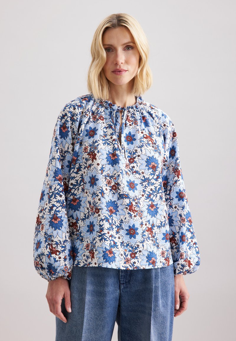 Blusa floreale con scollo arricciato, motivo floreale blu e rosso su sfondo bianco, maniche lunghe e vestibilità comoda.