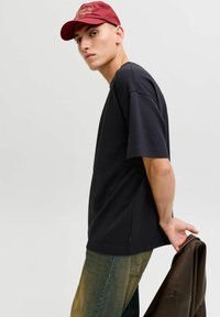 Črna bombažna majica s kratkimi rokavi, sproščen kroj, bočni razporki. Oblečena z zbledelimi zelenimi kavbojkami in drži rjavo jakno. Rdeča kapa kot poudarek.