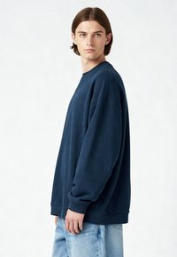 Tamsiai mėlynas per didelis džemperis, pagamintas iš minkštos medžiagos, su apvalia iškirpte, nuleistais petimis ir galuose bei apykaklėje prisiūtomis ипльм. Dėvimas su šviesiai mėlynomis džinsomis.