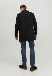 Cappotto nero con design strutturato, colletto e maniche lunghe, abbinato a jeans blu e scarpe nere, caratterizzato da una consistenza liscia.