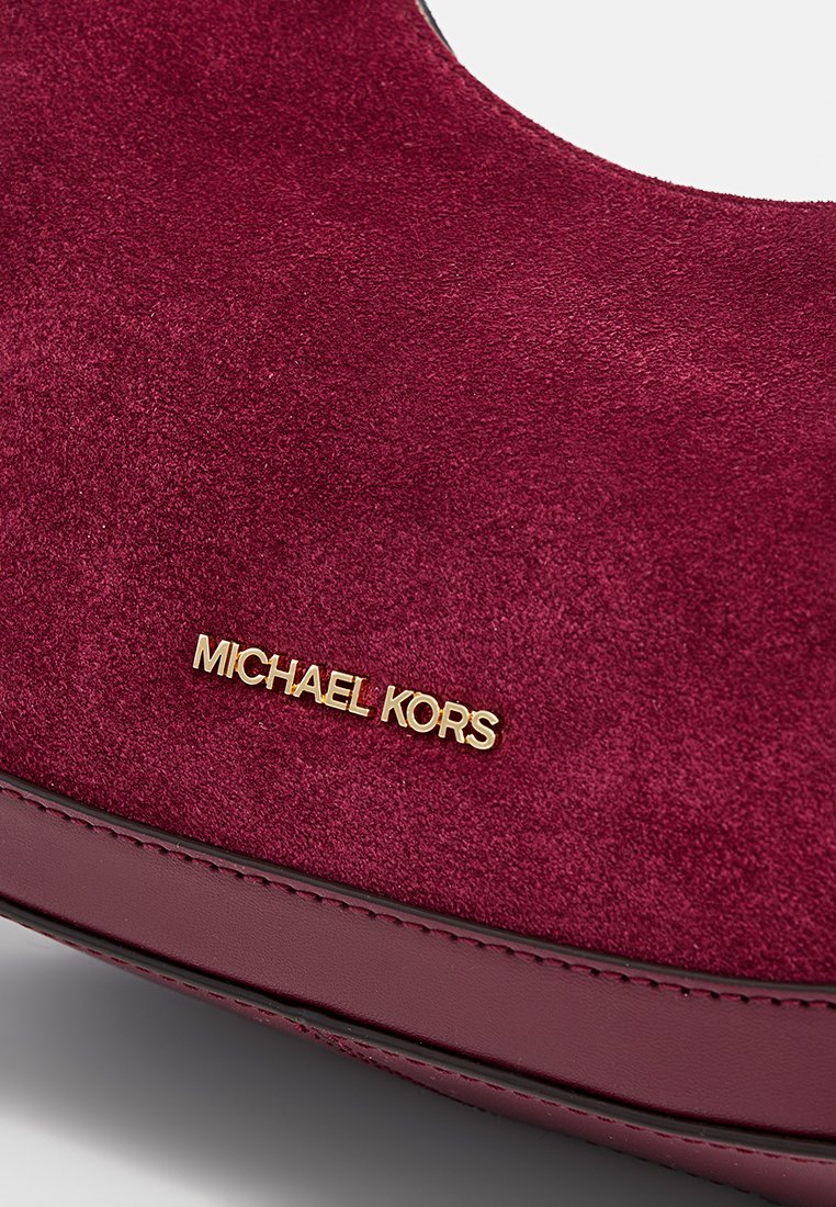 Flats en daim bordeaux avec un bout arrondi ; présente un logo doré "MICHAEL KORS" sur le côté et un contour en cuir lisse autour de la semelle.