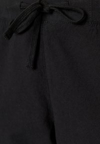 Gros plan sur un tissu noir montrant un cordon de serrage noué et les détails des coutures d'un vêtement, probablement un pantalon de survêtement ou un short.