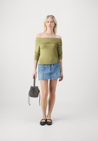 Oliven av-shoulder topp, trekvart ermer, kombinert med en denim mini skjørt med frayskant. Tilbehør med en mønstret svart bøtteveske.