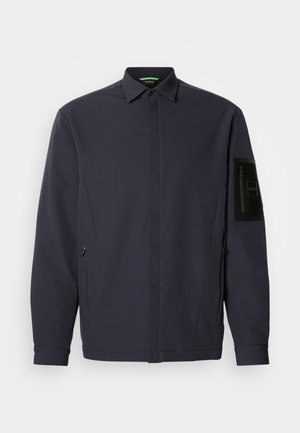 Donkerblauwe buitenjas met een gestructureerd ontwerp, voorzien van een puntige kraag, een zijzak met rits en een ritssluiting aan de linkermouw.