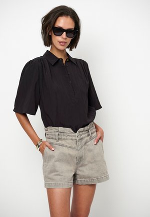 Zwart shirt met korte mouwen en een button-down kraag, gecombineerd met hooggesneden grijze denim shorts. Model draagt zwarte cat-eye zonnebril.