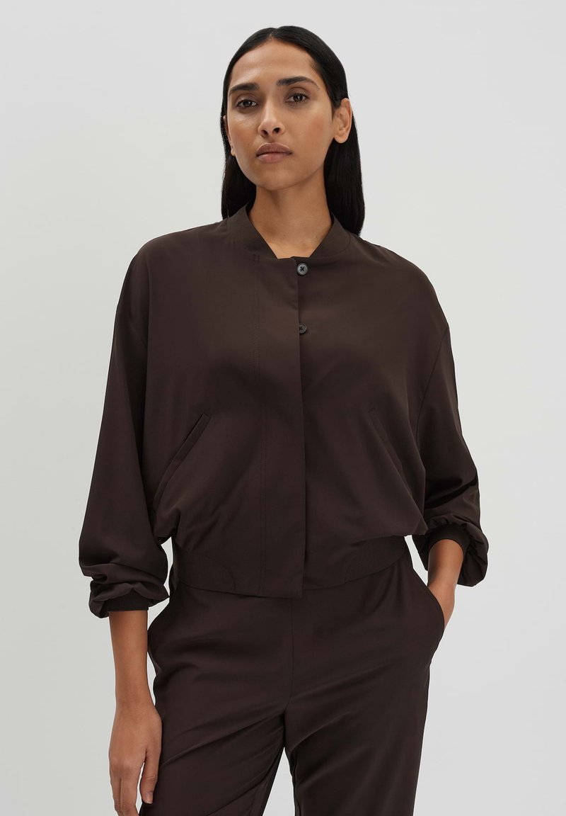 Brown cropped jacket in smooth fabric, featuring a stand collar, front button closure, and side pockets with gathered sleeves and cuffs.