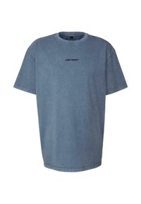 Zils pārāk liels T-krekls ar melnu tekstu "LOST YOUTH", kas centrēts krūšu daļā, ar apaļu kakla izgriezumu un īsām piedurknēm.