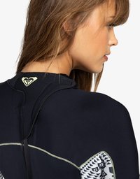 Neopreno negro con un diseño ajustado, que presenta un patrón tribal blanco en la manga y un detalle de logo en la parte trasera. Textura suave.