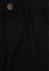 Čierne bavlnené nohavice s hladkým povrchom, vybavené hnedým gombíkom, skladaným predným dielom a bočnou vreckom. Jednoduchý a funkčný dizajn.