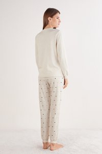 Beżowa bluzka z długim rękawem i okrągłym dekoltem, zestawiona z jasnoszarymi spodniami do spania z małymi czarnymi serduszkami, wykonanymi z miękkiego materiału.