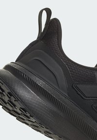 Schwarzer Sportschuh mit strukturiertem Obermaterial, glatten Überzügen und einer dicken, gemusterten Gummisohle mit ausgeprägtem Profil und einem Zuglasche.