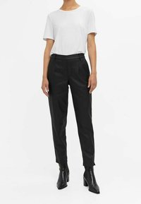 Pantalons noirs près du corps avec une taille plate, ourlet à revers et poches latérales, associés à un t-shirt blanc uni à manches courtes et des bottes à talons noires.