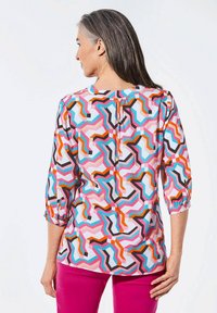 Mehrfarbige Bluse mit geometrischem Muster in Rosa, Orange, Blau und Schwarz; Dreiviertelärmel und runder Halsausschnitt mit leichter Raffung am Rücken.