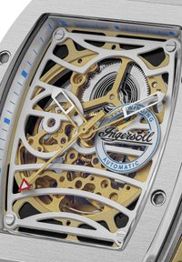 Automatische Uhr in Silber und Gold mit einem Skelettdesign; filigrane Zahnräder, blaue Akzente und Logodetail auf einem transparenten Zifferblatt.