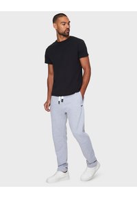 Zwarte t-shirt met korte mouwen, gecombineerd met lichtgrijze sweatpants met zijzakken en een trekkoord, gedragen met witte sneakers.
