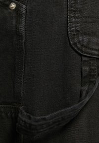 Tissu en denim noir mettant en valeur un gros plan d'une poche latérale avec des accessoires en argent, un tissage texturé et un détail de couture visible.