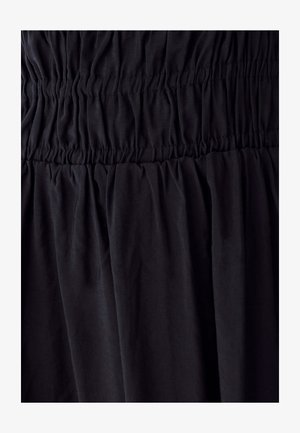 Melnas auduma kleita ar savilktām detaļām, ar teksturētu izskatu un plūstošu siluetu. Papildu raksti vai akcenti nav redzami.