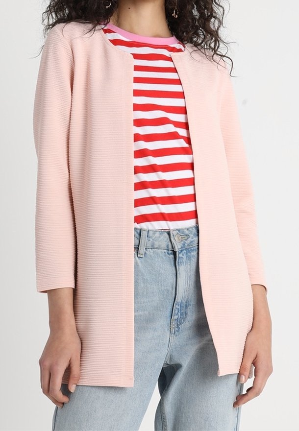 Ljusrosa texturerad cardigan med trekvartsärmar, bärs över en röd och vit randig skjorta, ihop med ljusblå jeans.