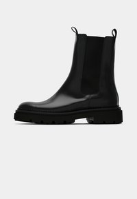 Svarta läderankelboots med elastiska sidopaneler, rund tå och tjock svart gummisula med mönstrad design.