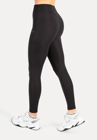 Zwarte leggings met hoge taille gemaakt van rekbaar materiaal, met een gladde textuur en een strakke pasvorm, gecombineerd met witte sportschoenen.