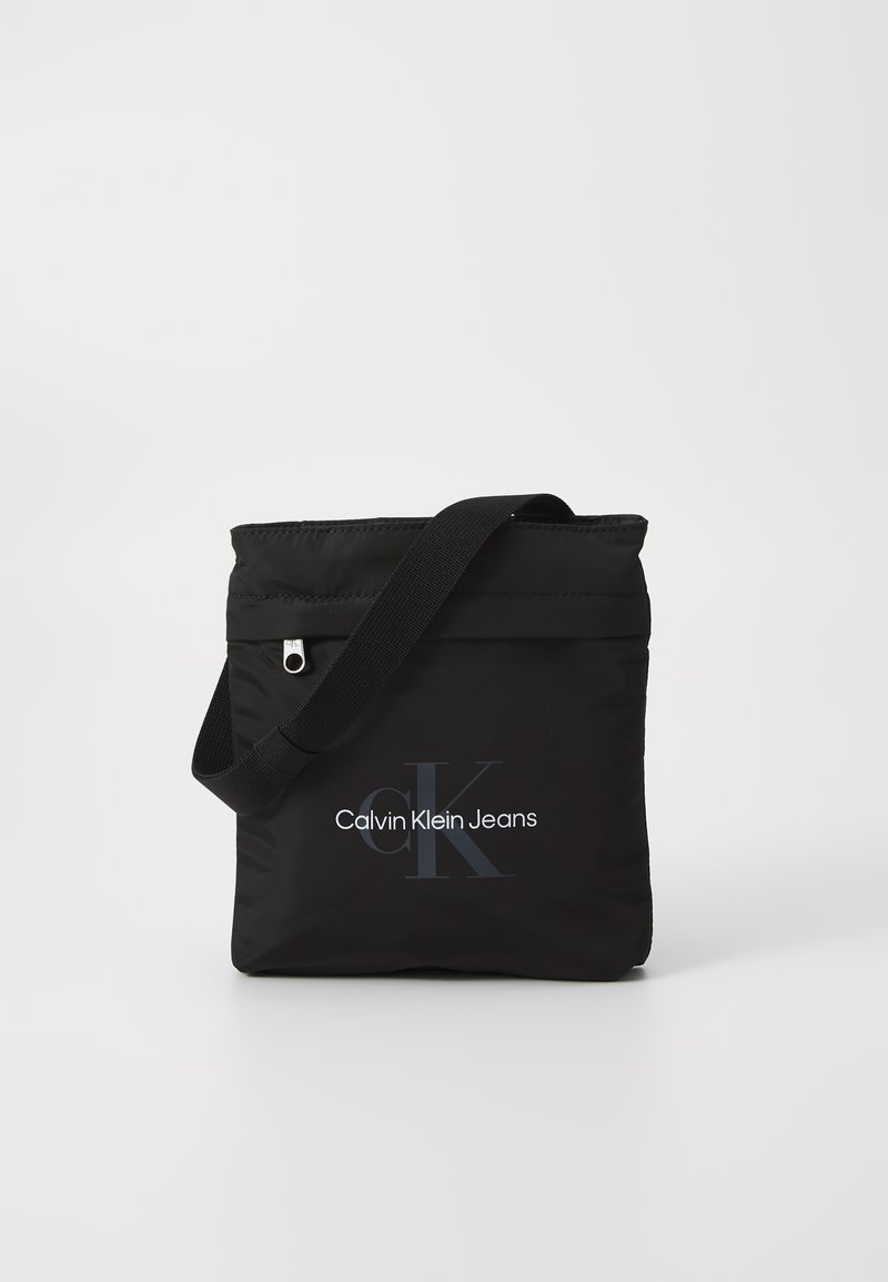 Borsa a spalla in nylon nero con tracolla regolabile, caratterizzata dal logo "Calvin Klein Jeans" in bianco e grigio sulla parte frontale.