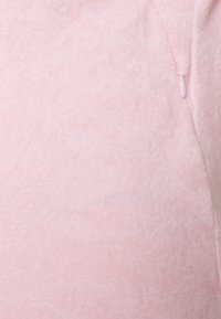 Tecido de fleece rosa claro com uma textura suave, apresentando um pequeno fecho de zíper de um lado. Mostra uma superfície lisa e uniforme.