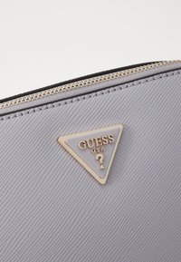 Gray textured material zip pouch featuring a triangular gold-tone logo accent with "GUESS USA" text. Zipper closure along the top edge.